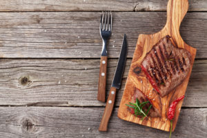 Grilled beef steak with rosemary, salt and pepper on wooden table.