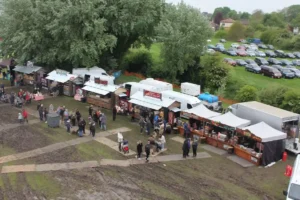 line of food shacks on muddy field, with car park in background