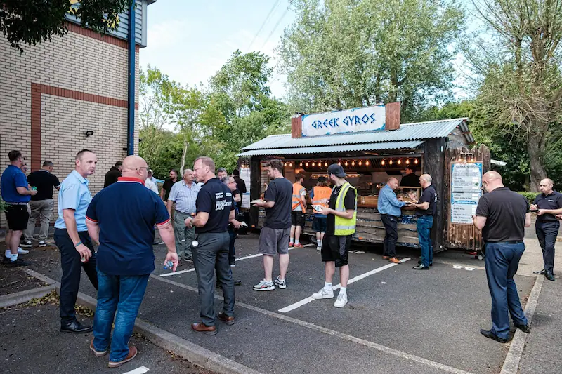 People gathered around a Greek gyros catering stall at an outdoor event